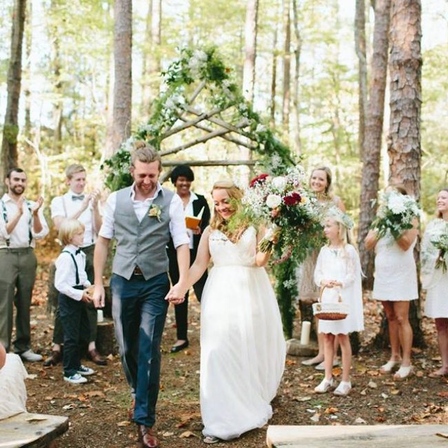 wedding couple walking down woodland ceremony isle with wedding party in the background