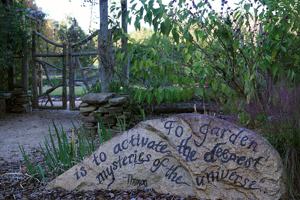 detailed shot of large boulder with the words written "To garden is to activate the deepest mysteries of the universe." quote by Thomas Berry